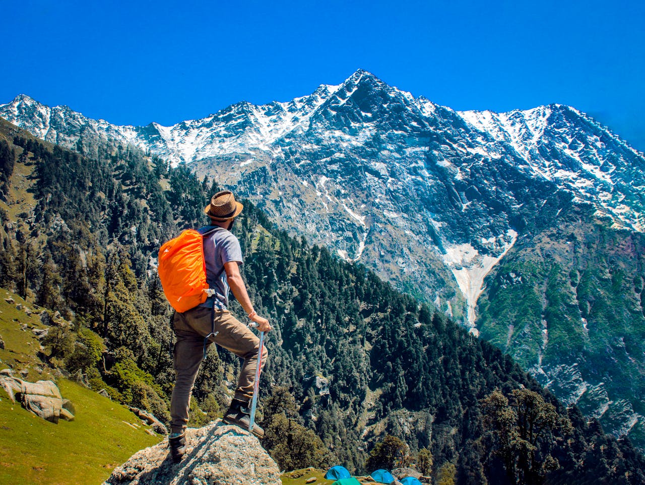 Man exploring breathtaking mountain scenery with snow-capped peaks under a clear blue sky.