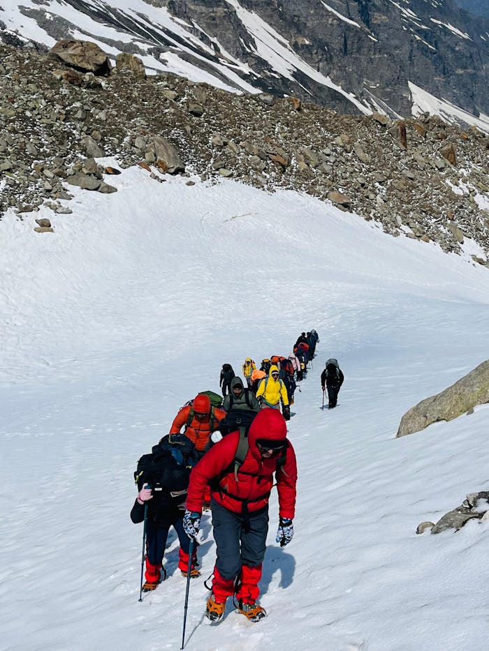 Group of trekkers hiking through snowy terrain in Hampta Pass, India.